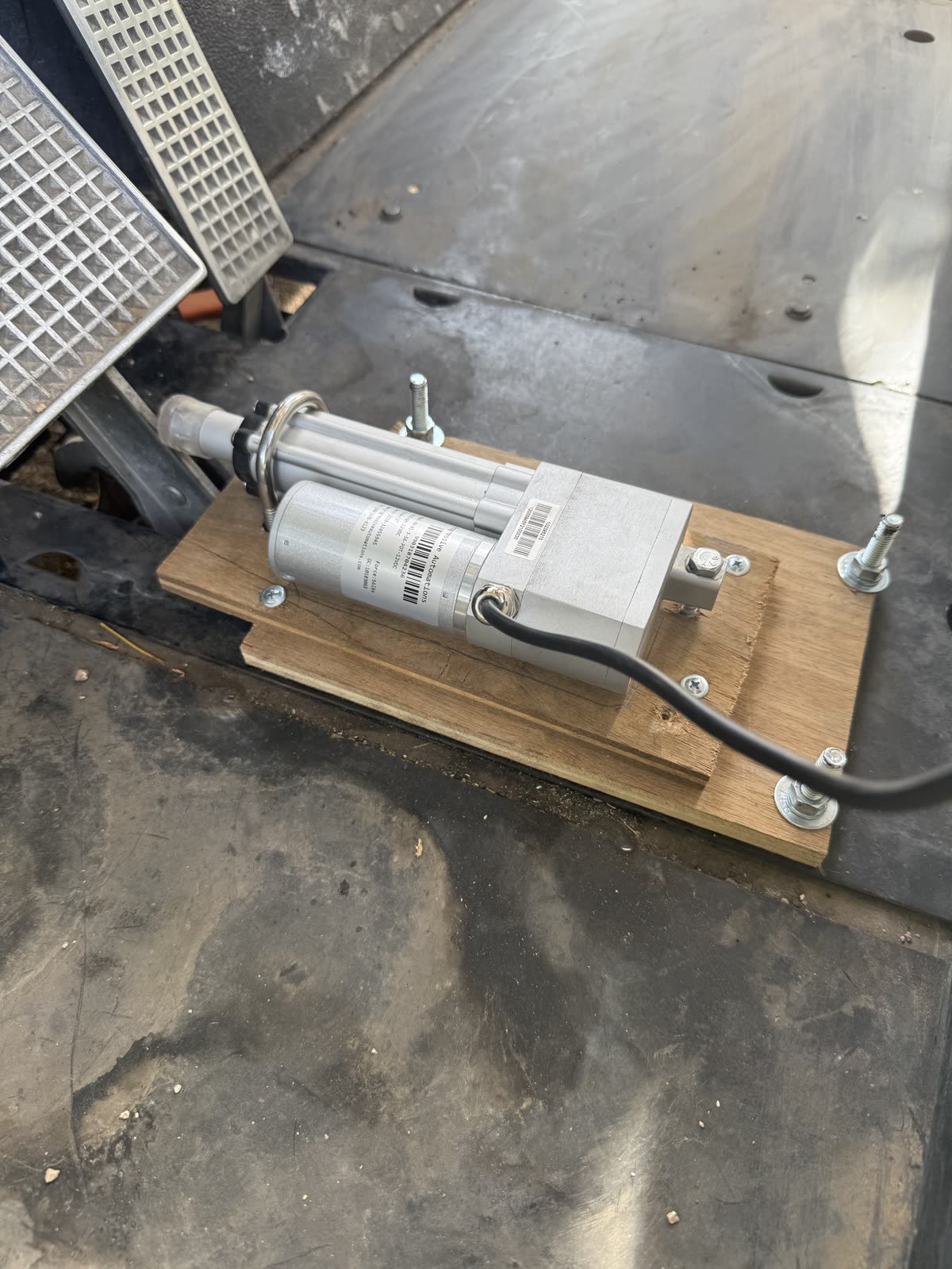 A linear actuator bolted to a wooden plate on the cart's floor, its rod pointing at the brake pedal