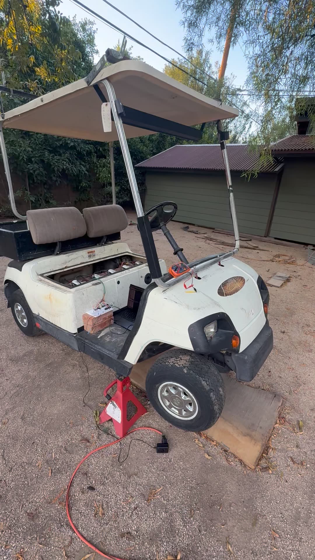 White Yamaha G22E golf cart with its rear on a red jackstand, electronics and a laptop on the floorboard