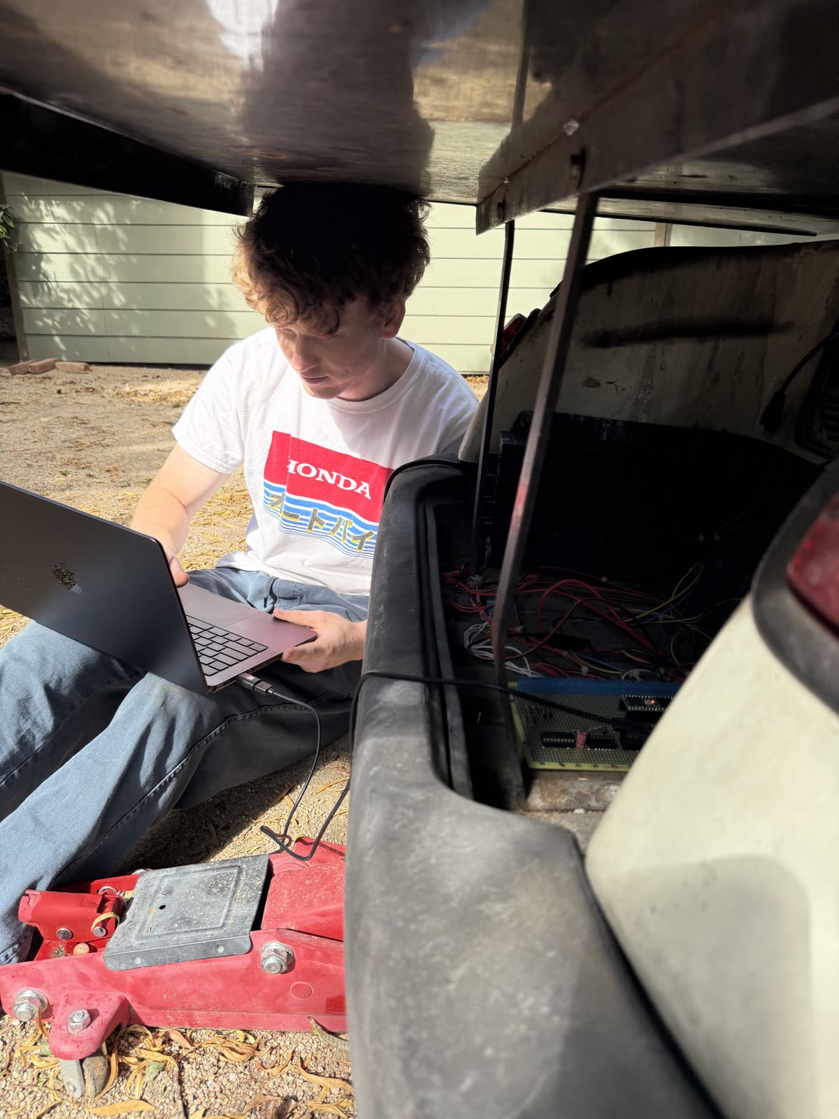 Jacob sitting beside the cart with a laptop, seen under the cart bed, with the electronics bay visible behind